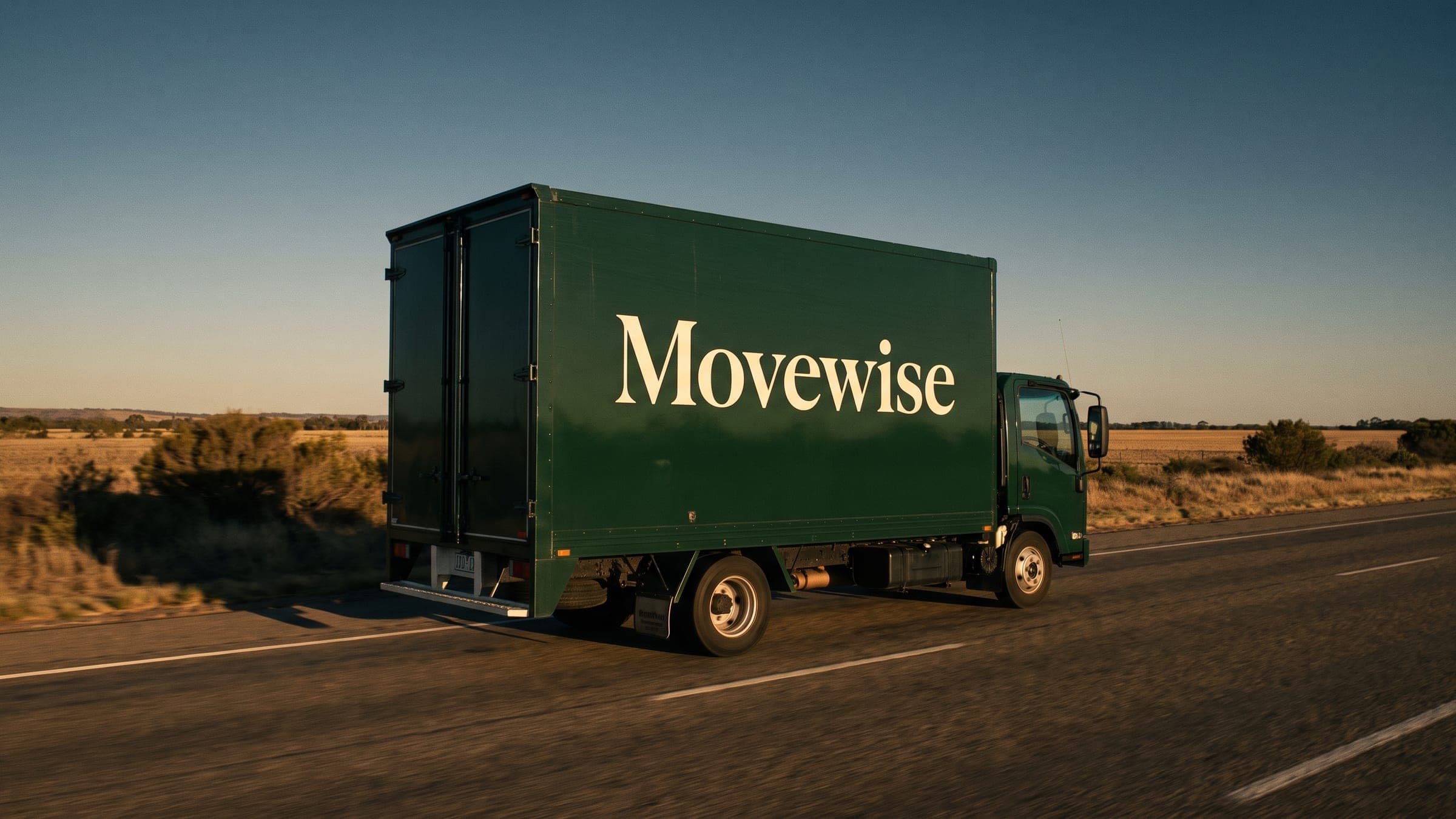 A Movewise truck on an open highway through dry scrub at golden hour.